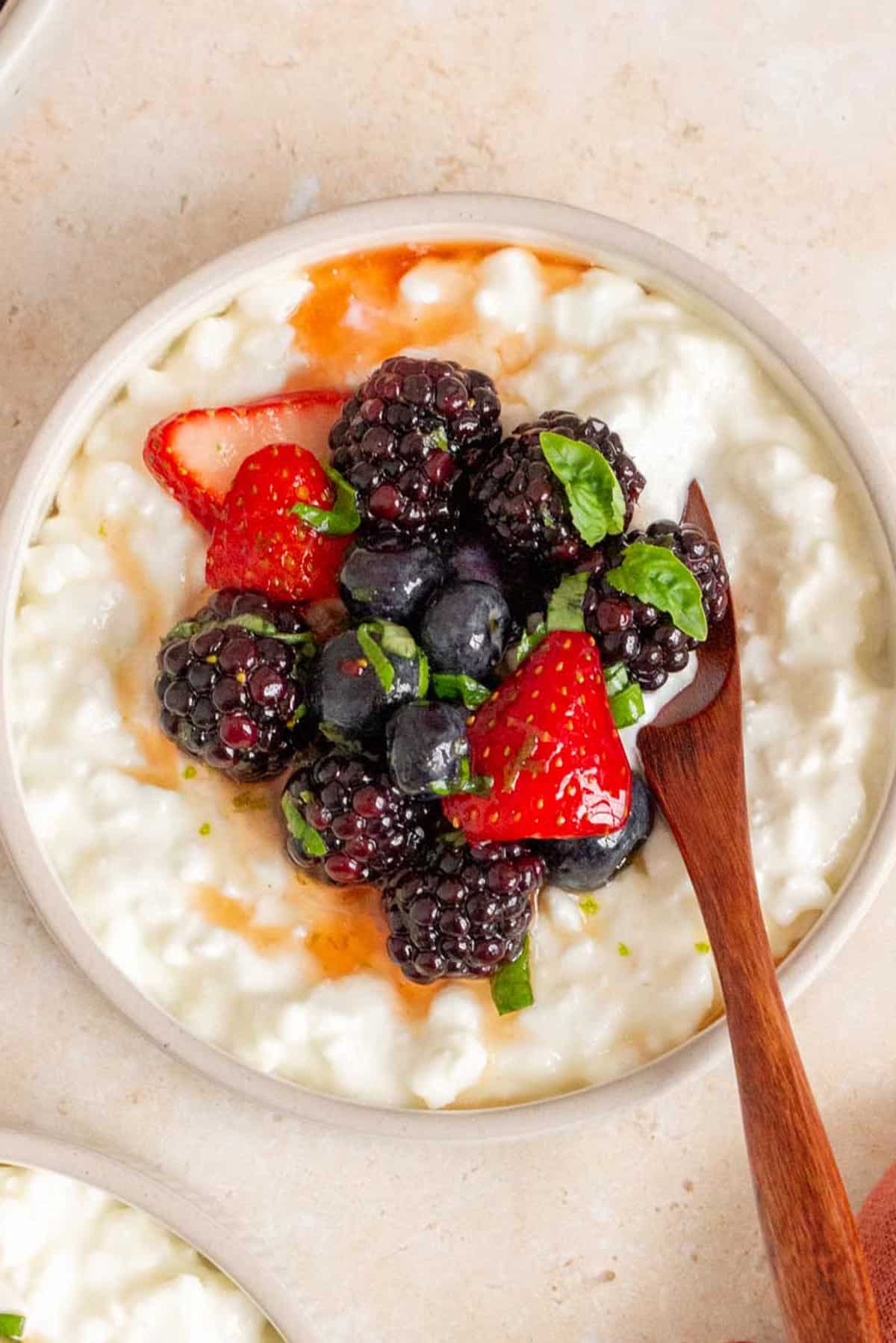 A plate of cottage cheese with fruit with a wooden spoon inserted.