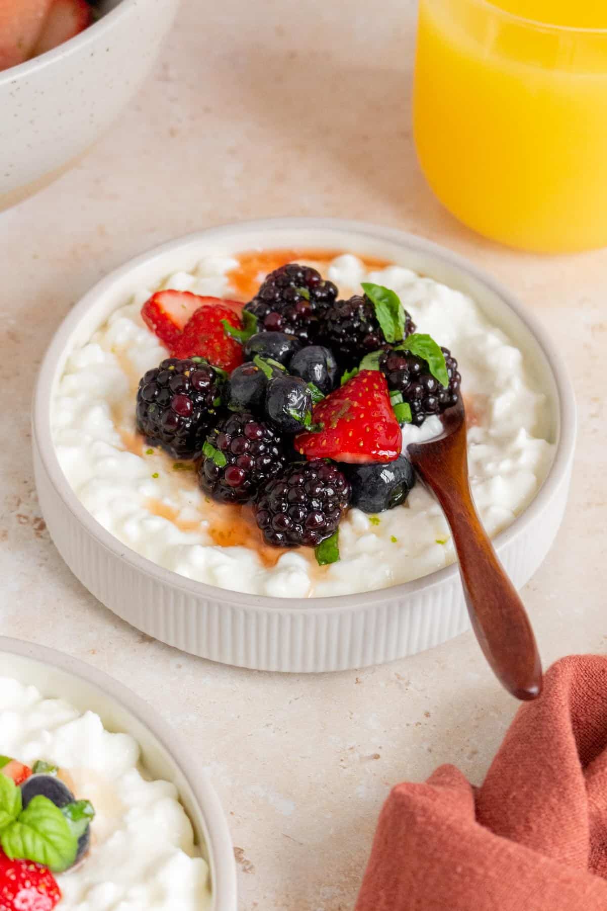 A plate of cottage cheese with fruit with a spoon inserted.