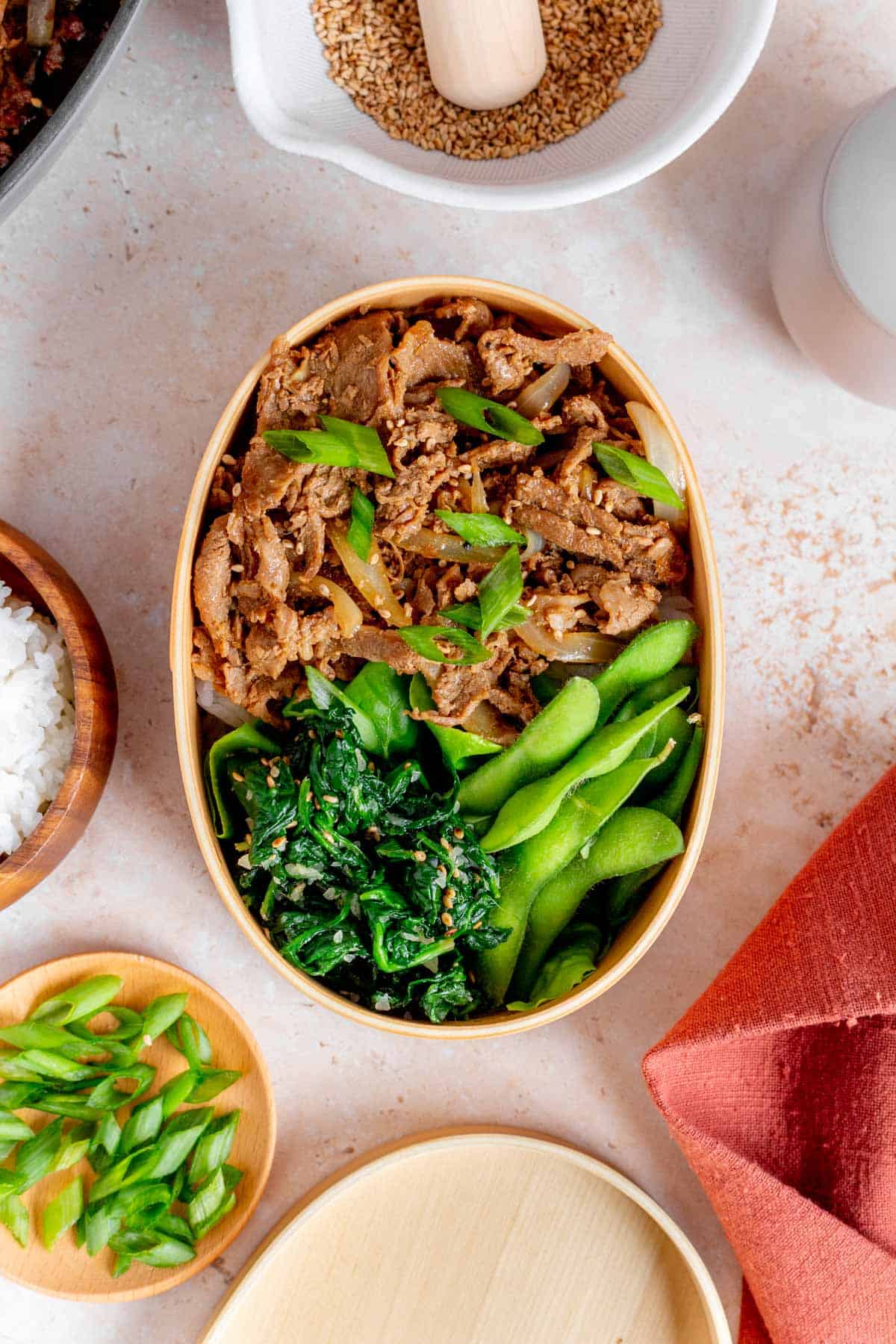 A bento box with ginger pork, spinach, edamame, and green onions.