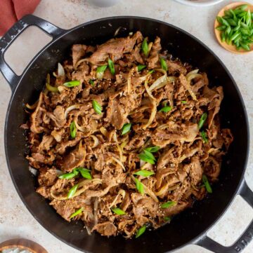 Overhead view of ginger pork in a skillet topped with green onions and toasted sesame seeds.