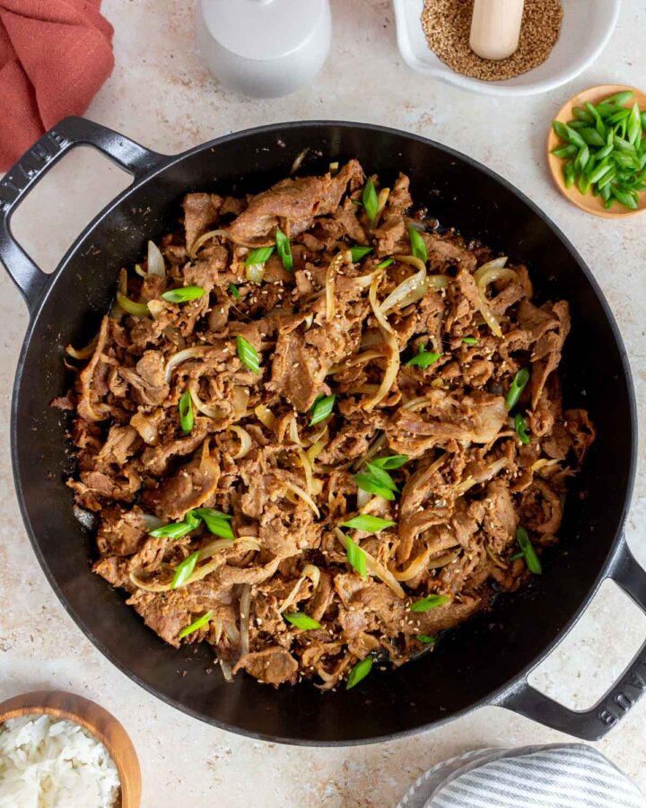 Overhead view of ginger pork in a skillet topped with green onions and toasted sesame seeds.