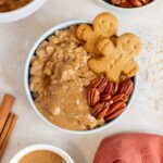 Overhead view of a bowl of gingerbread oatmeal topped with gingerbread cookies, pecans, and almond butter.