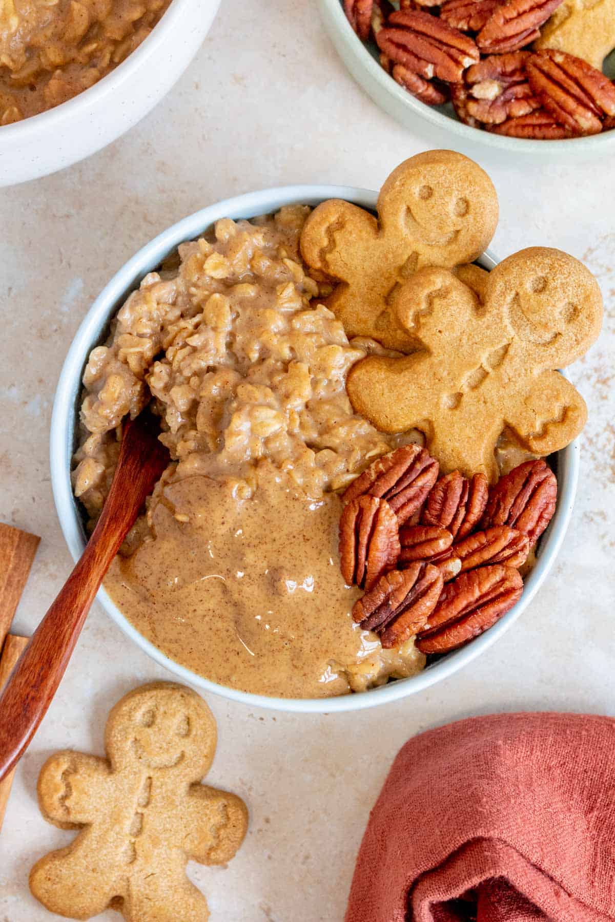Overhead view of a bowl of gingerbread oatmeal topped with gingerbread cookies, pecans, and almond butter with a spoon inserted.
