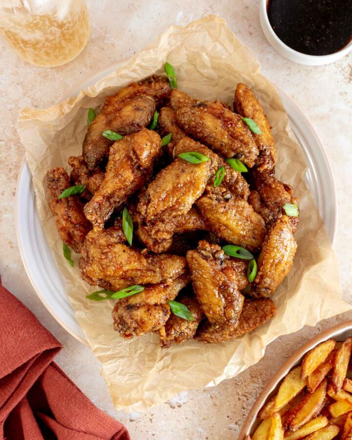 An overhead view of a plate of honey soy chicken wings topped with green onions.