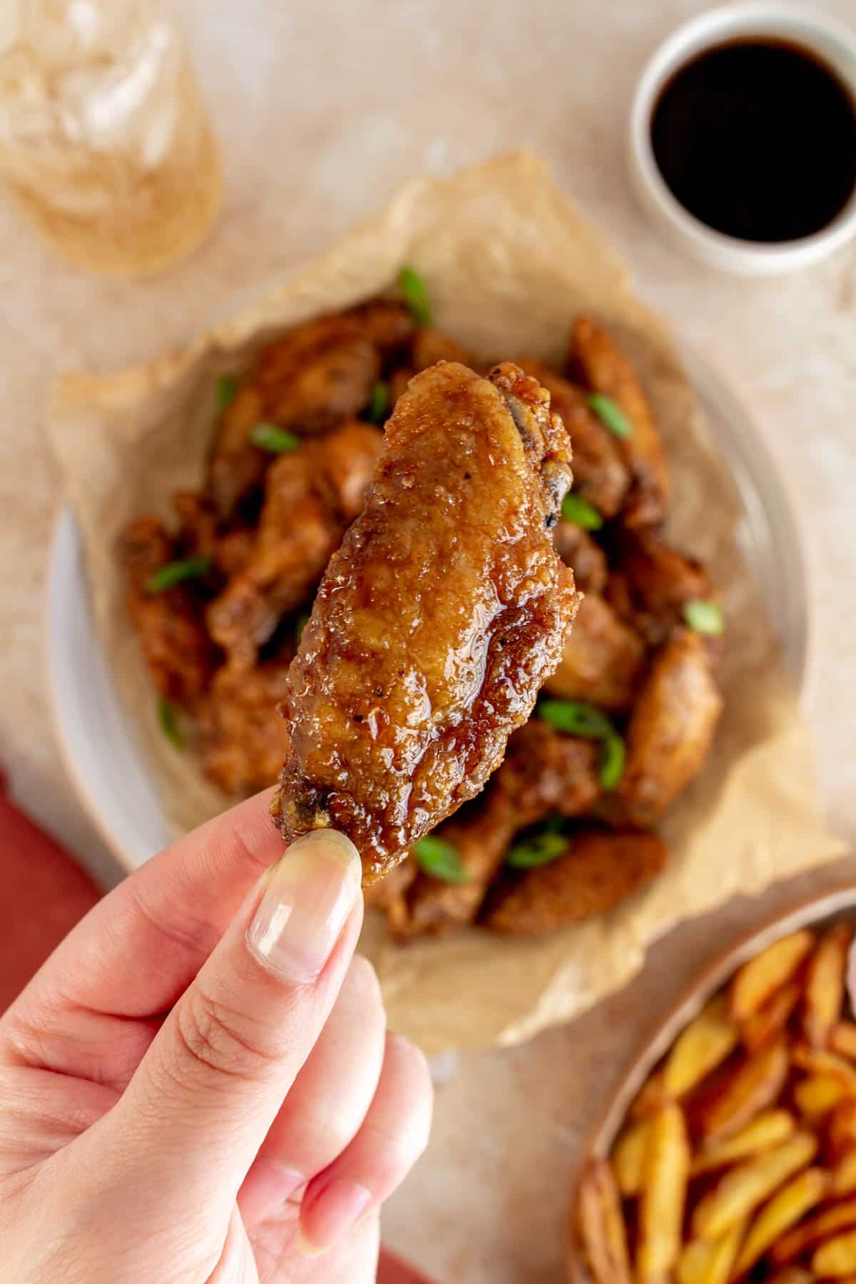 A hand holding up a honey soy chicken wing over a plate of more wings.