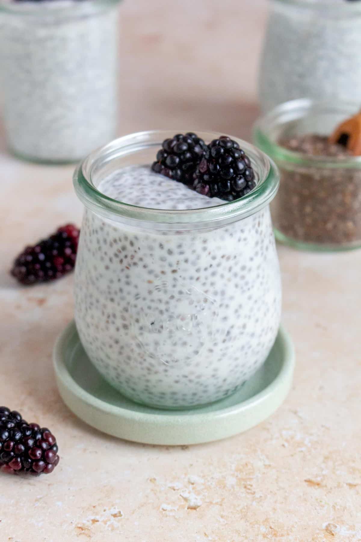 A jar of kefir chia pudding topped with blackberries and more scattered around.