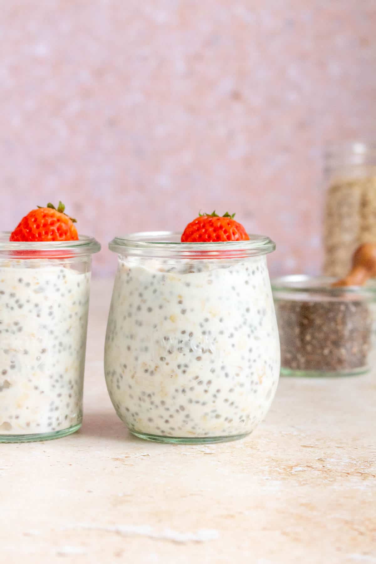 Two jars of kefir overnight oats topped with a mini strawberry.