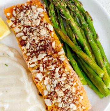 A close view of a plate with almond crusted salmon, asparagus, mashed potatoes, and a lemon wedge.