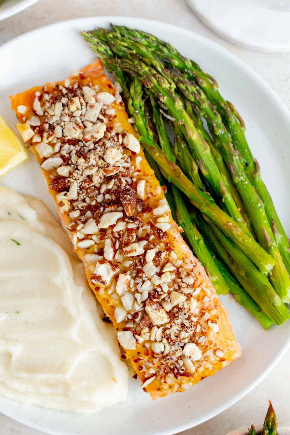 A close view of a plate with almond crusted salmon, asparagus, mashed potatoes, and a lemon wedge.
