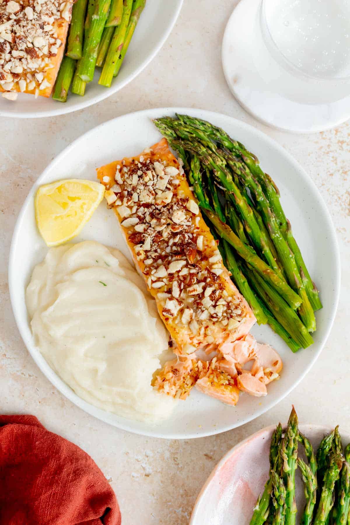 A plate with almond crusted salmon where part of it is flaked on a plate along with a lemon wedge, mashed potatoes, and asparagus.