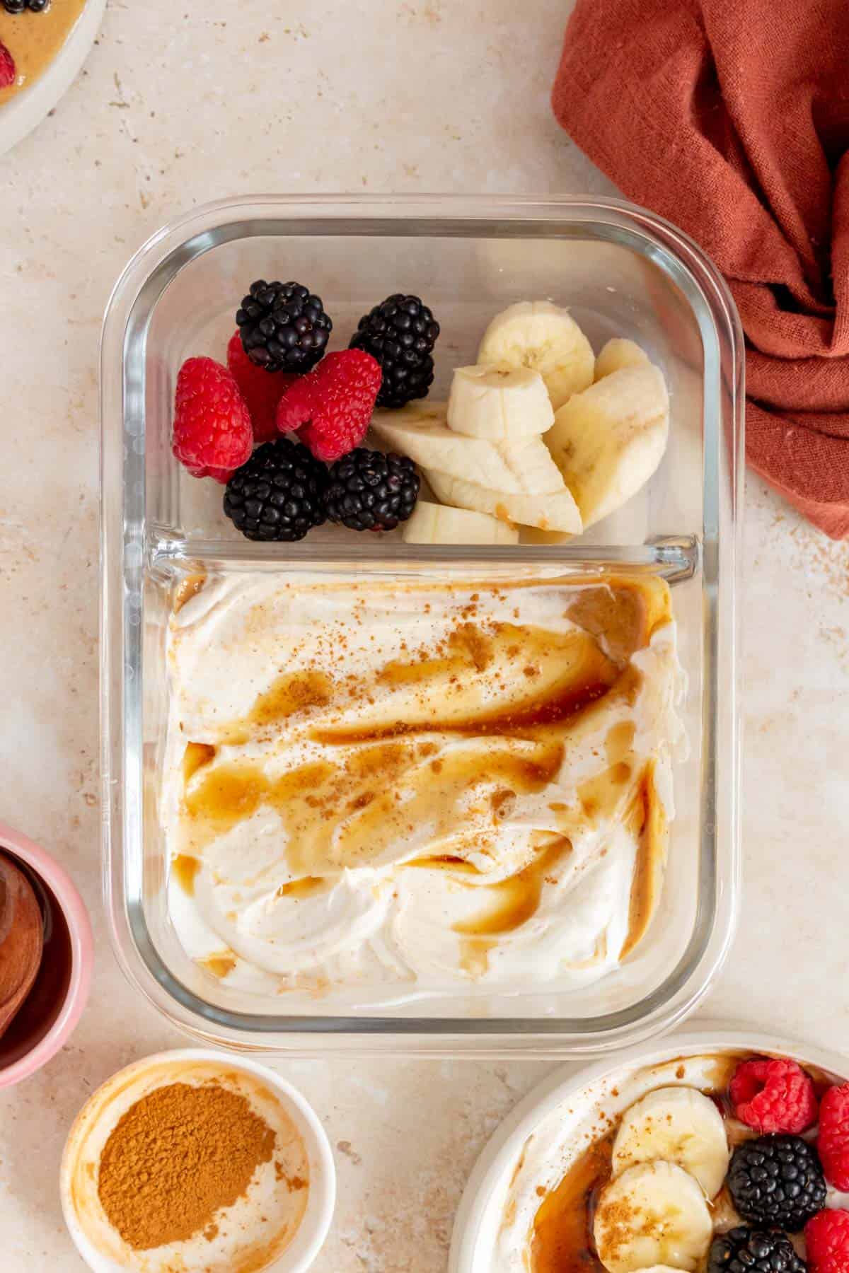 Greek yogurt peanut butter in a meal prep container along with berries and banana slices.