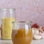 A jar of nutritional yeast dressing with a jar of nutritional yeast and garlic cloves in the background.