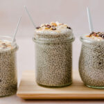 A jar of peanut butter chia pudding topped with peanut butter and cocoa bits with two more beside it.