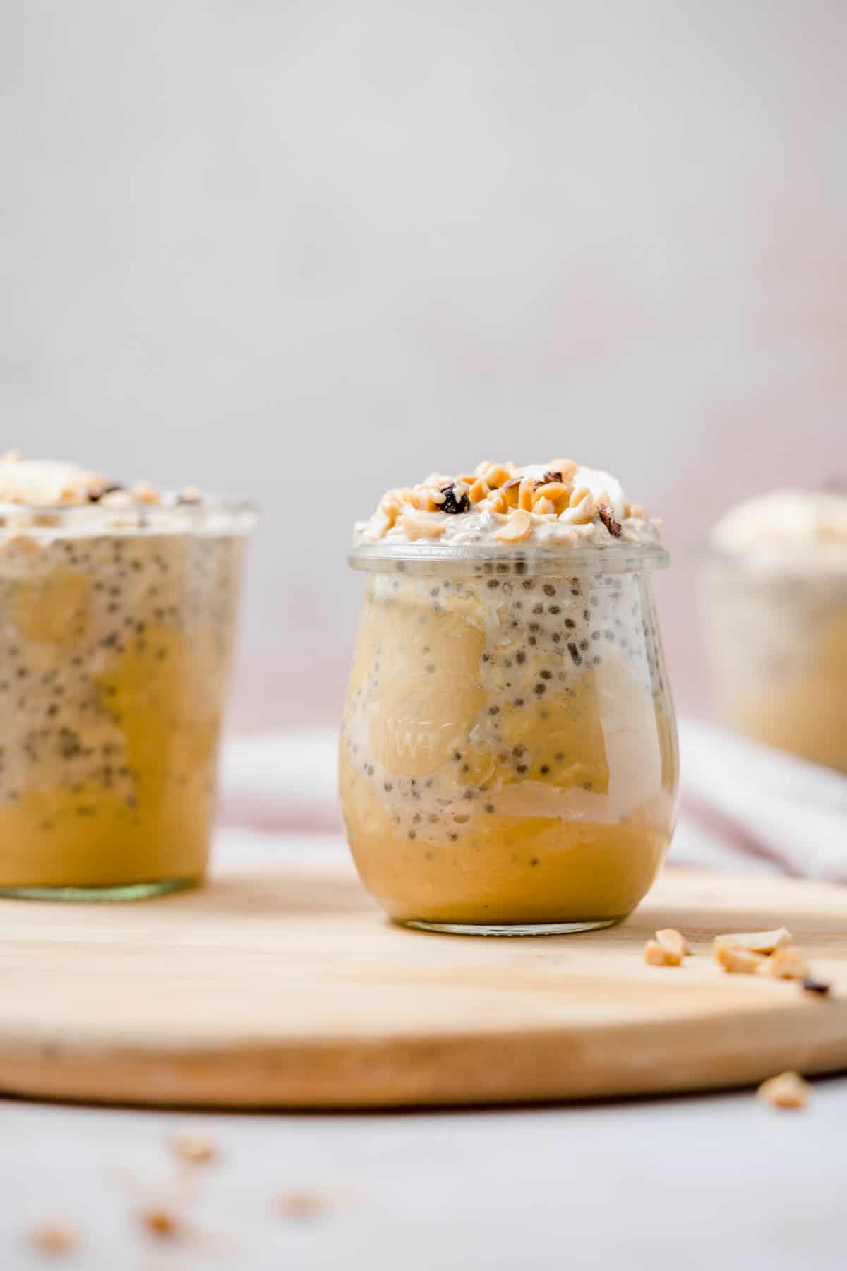 A jar of peanut butter banana overnight oats on a wooden board with a second out out of focus off to the side.