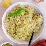 Overhead view of a plate of pesto rice with a spoon and basil garnish.