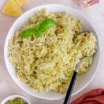 Overhead view of a plate of pesto rice with a spoon and basil garnish.