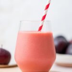 A glass of plum smoothie with a straw.