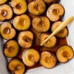 A baking dish of roasted plums with a spoon tucked under one plum.