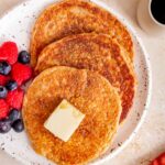 A close view of three cottage cheese oatmeal pancakes on a plate with syrup and a pat of butter with berries beside them.