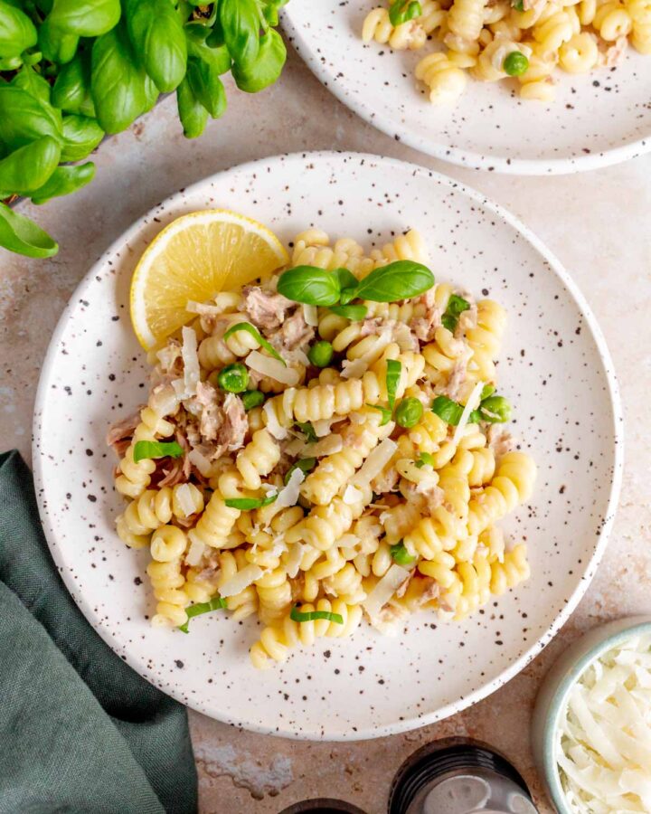 Overhead view of a plate of creamy tuna pasta with fresh basil and a slice of lemon.