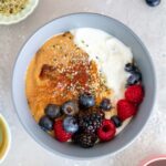 Close up view of Greek yogurt peanut butter bowl topped with fruit and hemp hearts surrounded by topping options.