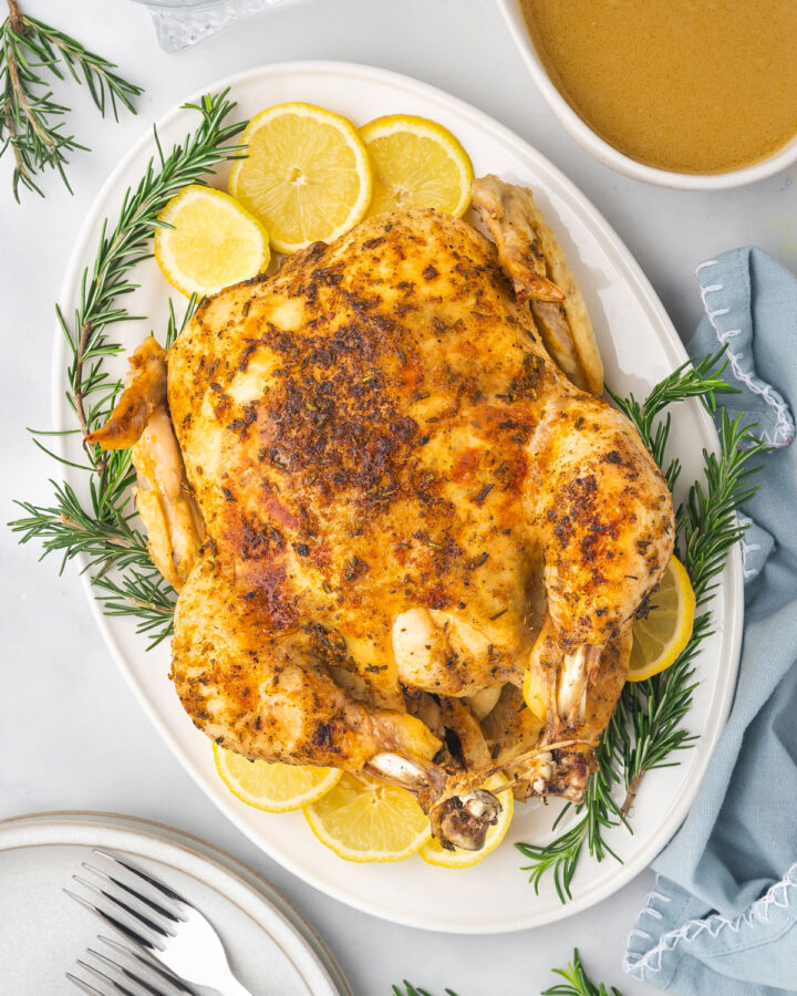 Overhead view of instant pot whole chicken on a platter surrounded by lemon slices and rosemary.