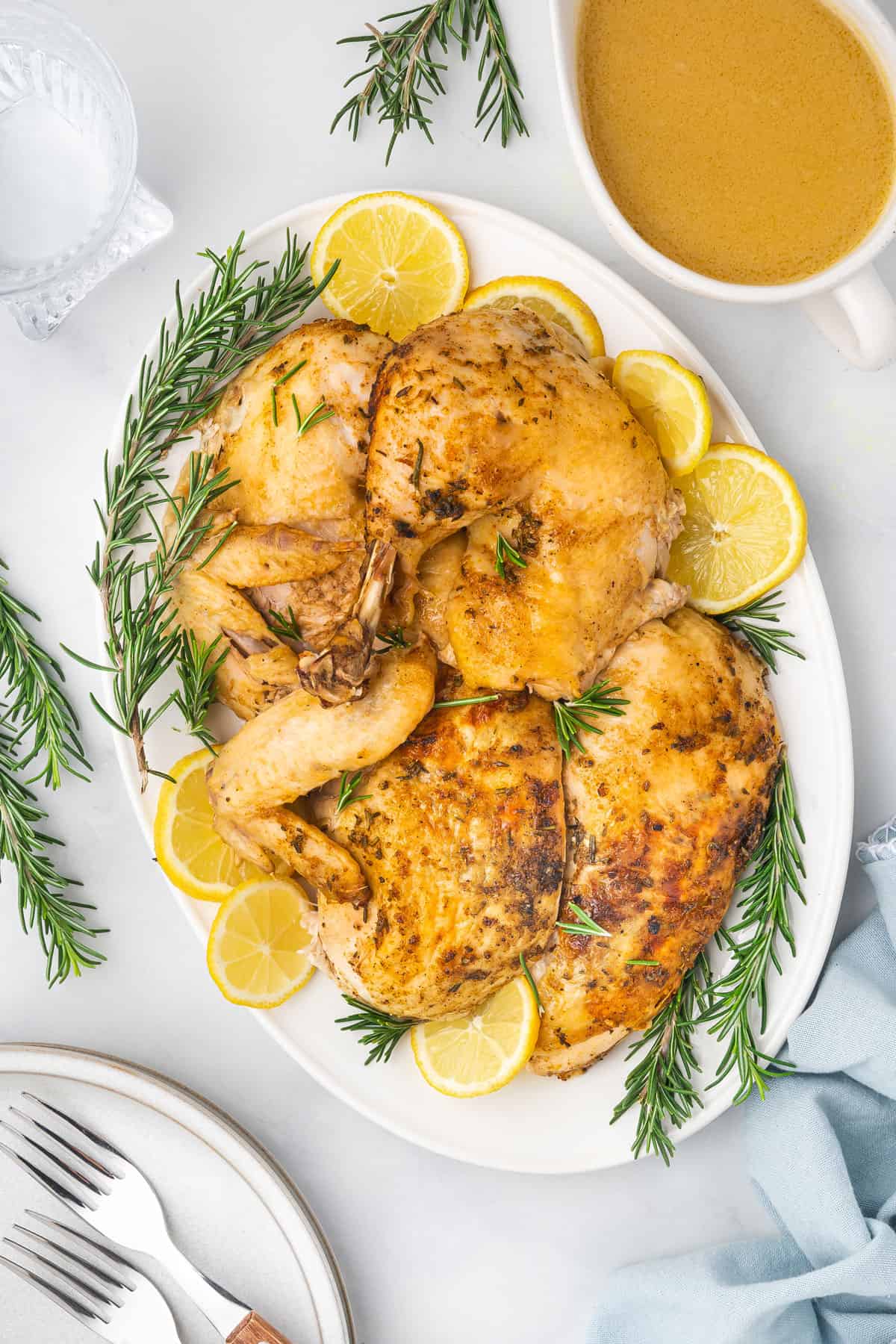 Overhead view of an instant pot whole chicken broken down on a platter surrounded by lemon slices and rosemary. Gravy off to the side.