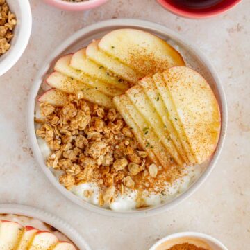 Overhead view of a cottage cheese apple cinnamon bowl surrounded by toppings in mini bowls.