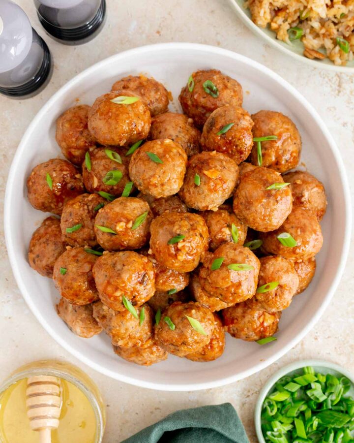 Overhead view of a plate of honey sriracha meatballs garnished with green onions.