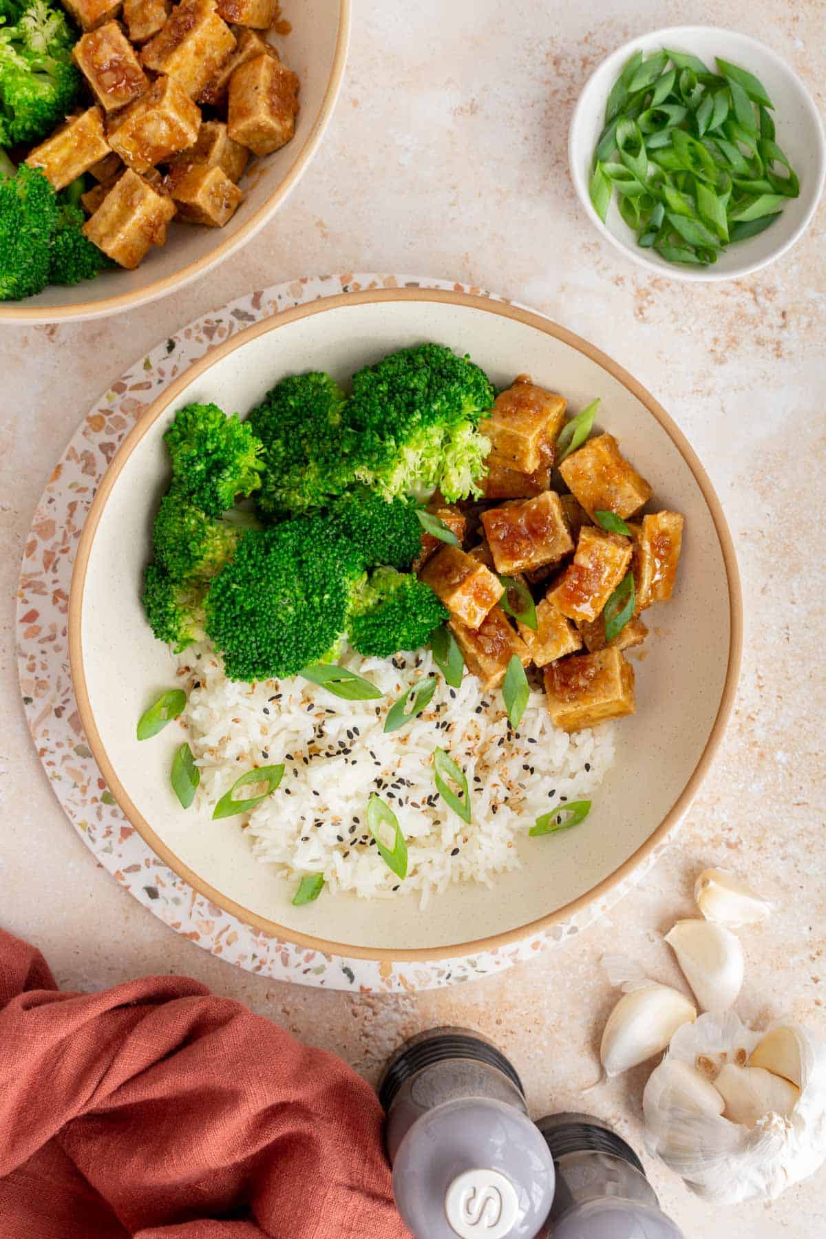 Overhead view of a bowl of honey garlic tofu with broccoli, rice, and green onions.