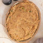A platter of refried beans surrounded by half a lime, a linen napkin, tortillas, and salt and pepper shakers.