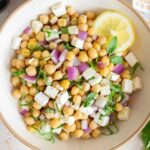 A close up view of a bowl of chickpea feta salad with a slice of lemon.