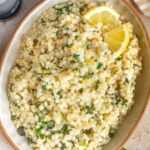 Overhead view of lemon herb couscous in an oval platter with two cuts of lemon slices.