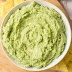 Overhead view of a bowl of 4 ingredient guacamole with tortilla chips and garlic scattered around.