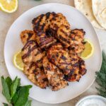 Overhead view of a platter of Greek yogurt marinated grilled chicken with lemon slices.