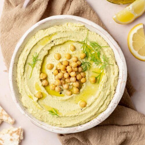 Lemon dill hummus in a bowl topped with chickpeas, olive oil, pepper, and dill.