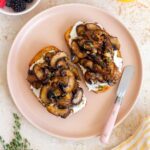 Overhead view of a plate with mushroom toast. Berries, orange juice, thyme, and a napkin off to the side.