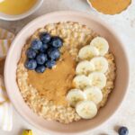 Overhead view of a bowl of peanut butter oatmeal with banana slices, peanut butter, and blueberries on top.
