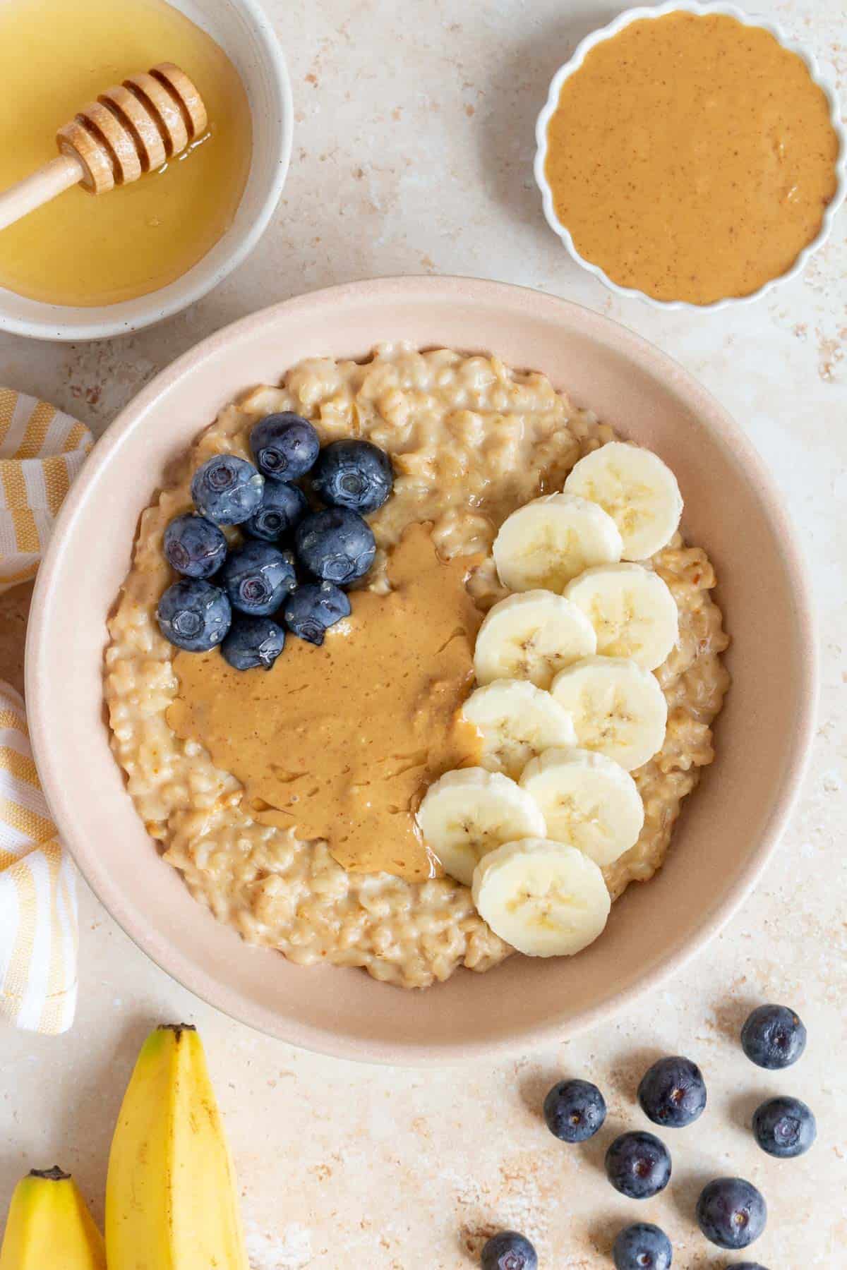 Overhead view of a bowl of peanut butter oatmeal with banana slices, peanut butter, and blueberries on top.
