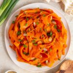 Overhead view of a plate of soy sesame raw carrot salad topped with green onions.
