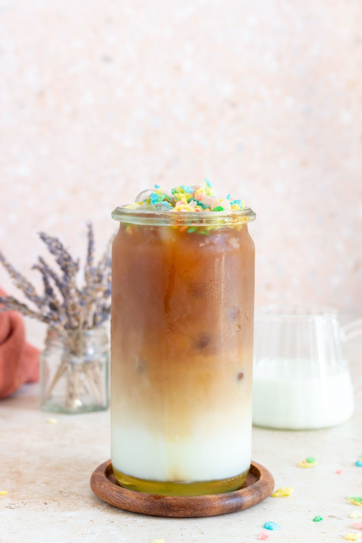 A glass of cereal milk latte with fruity pebbles on top.