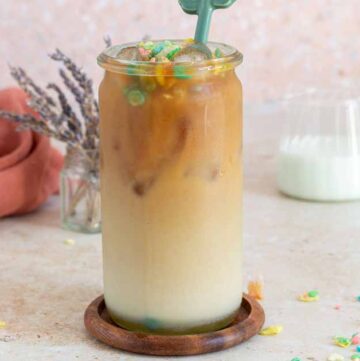 A glass of cereal milk latte with fruity pebbles on top.
