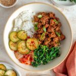 Overhead view of a gochujang ground beef bowl with rice, spinach, kimchi, and spicy cucumbers.
