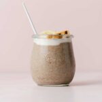 A glass of banana chia pudding with banana slices, walnuts, and a spoon.