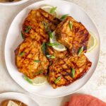 A platter with four Dijon mustard grilled pork chops with lemon slices and green onion garnish.