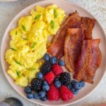 A plate of Greek yogurt scrambled eggs with bacon and berries.