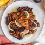 Overhead view of a platter of grilled honey sriracha chicken thighs with lemon slices.