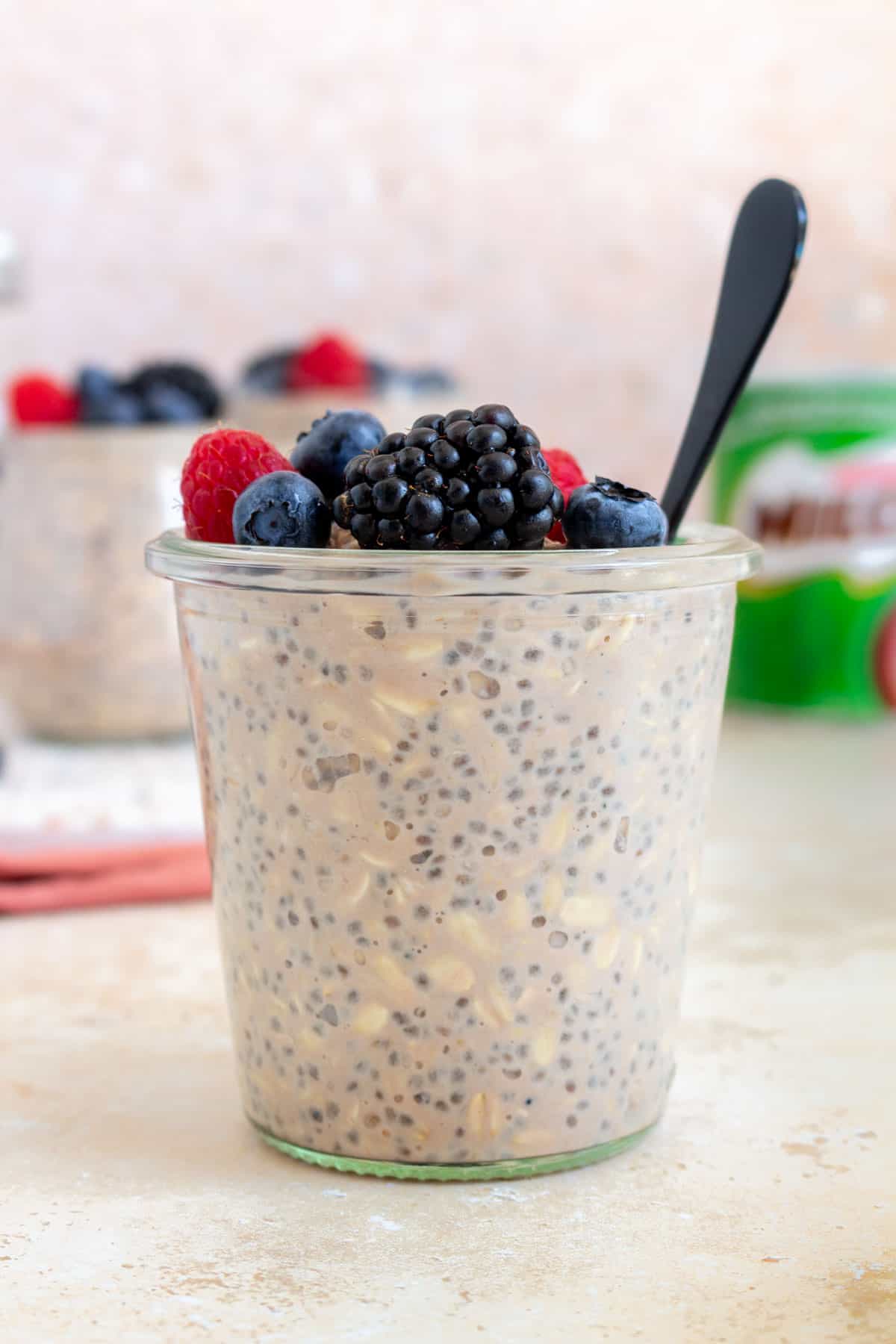 A jar of milo overnight oats topped with berries with a spoon.
