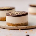 A profile view of a protein peanut butter cup on a plate with two more in the background, out of focus.