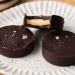A plate with three protein peanut butter cups with one stacked on top of two with a bite taken out.